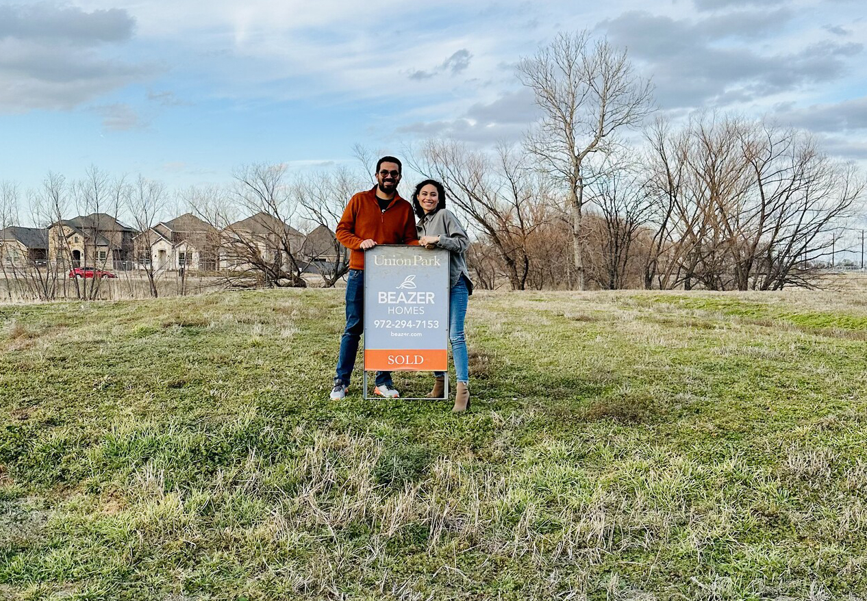 Couple standing with sold sign on empty lot