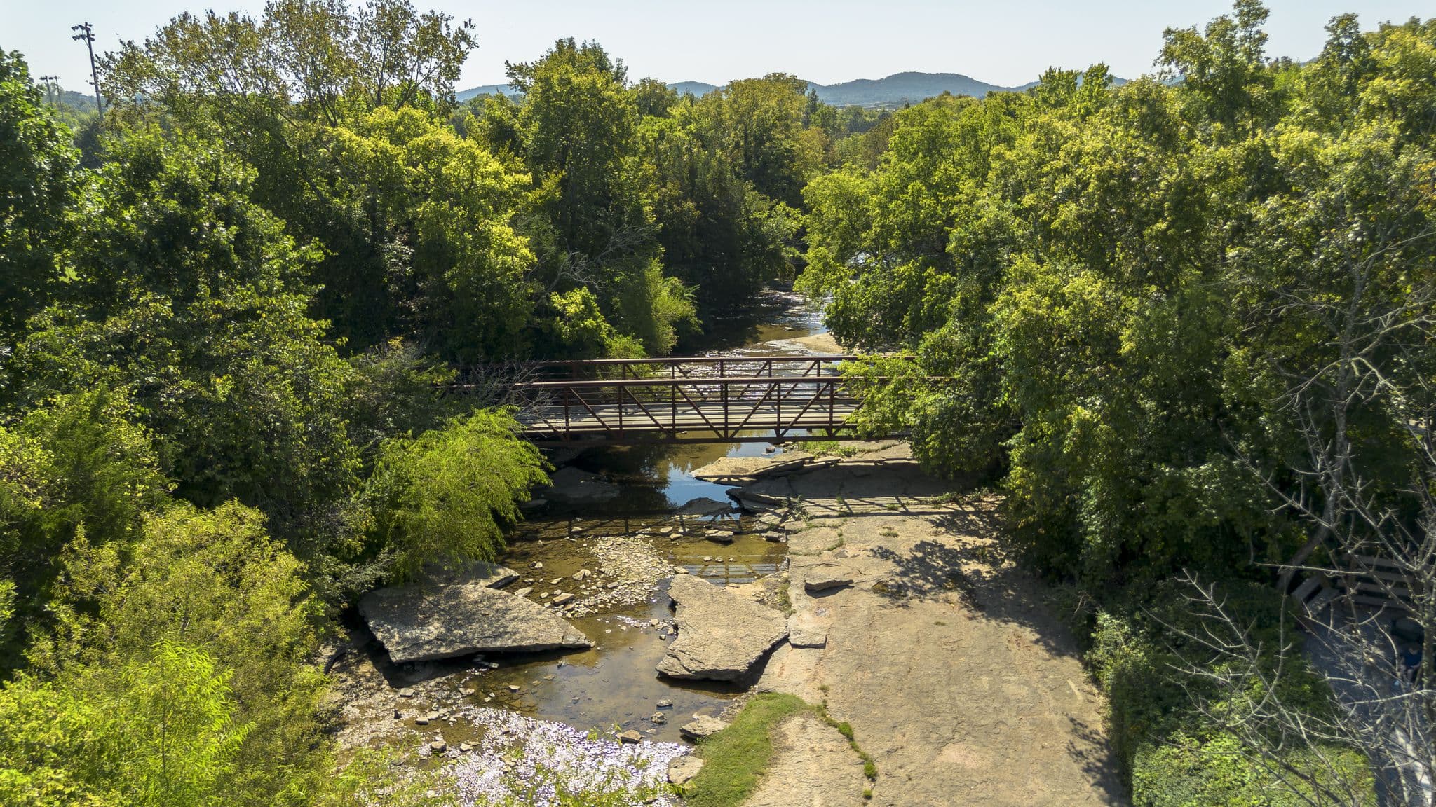 tree-filled park with natural rock, a creek, and a bridge going across the water