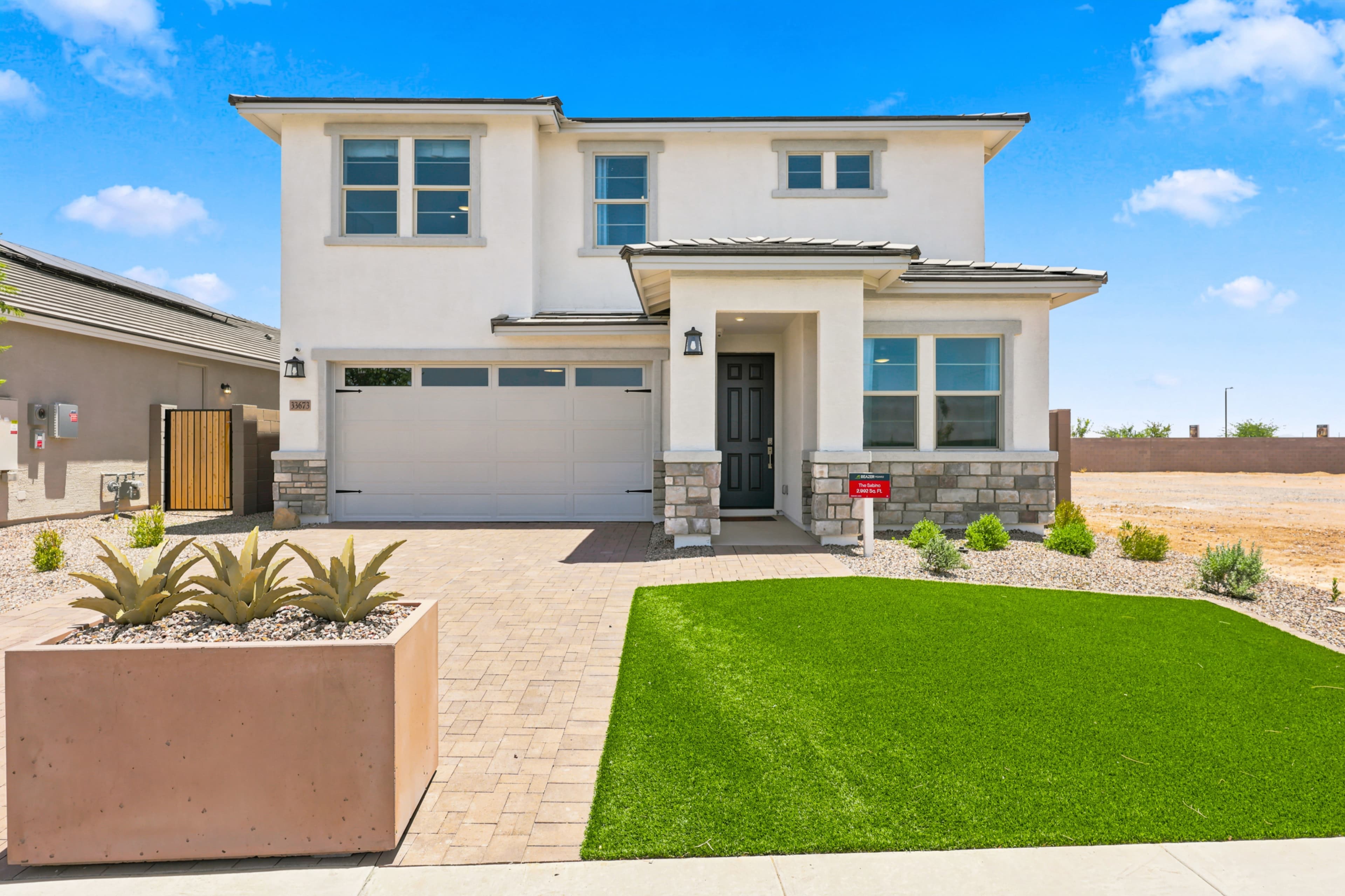 two-story home with paver driveway and artificial turf