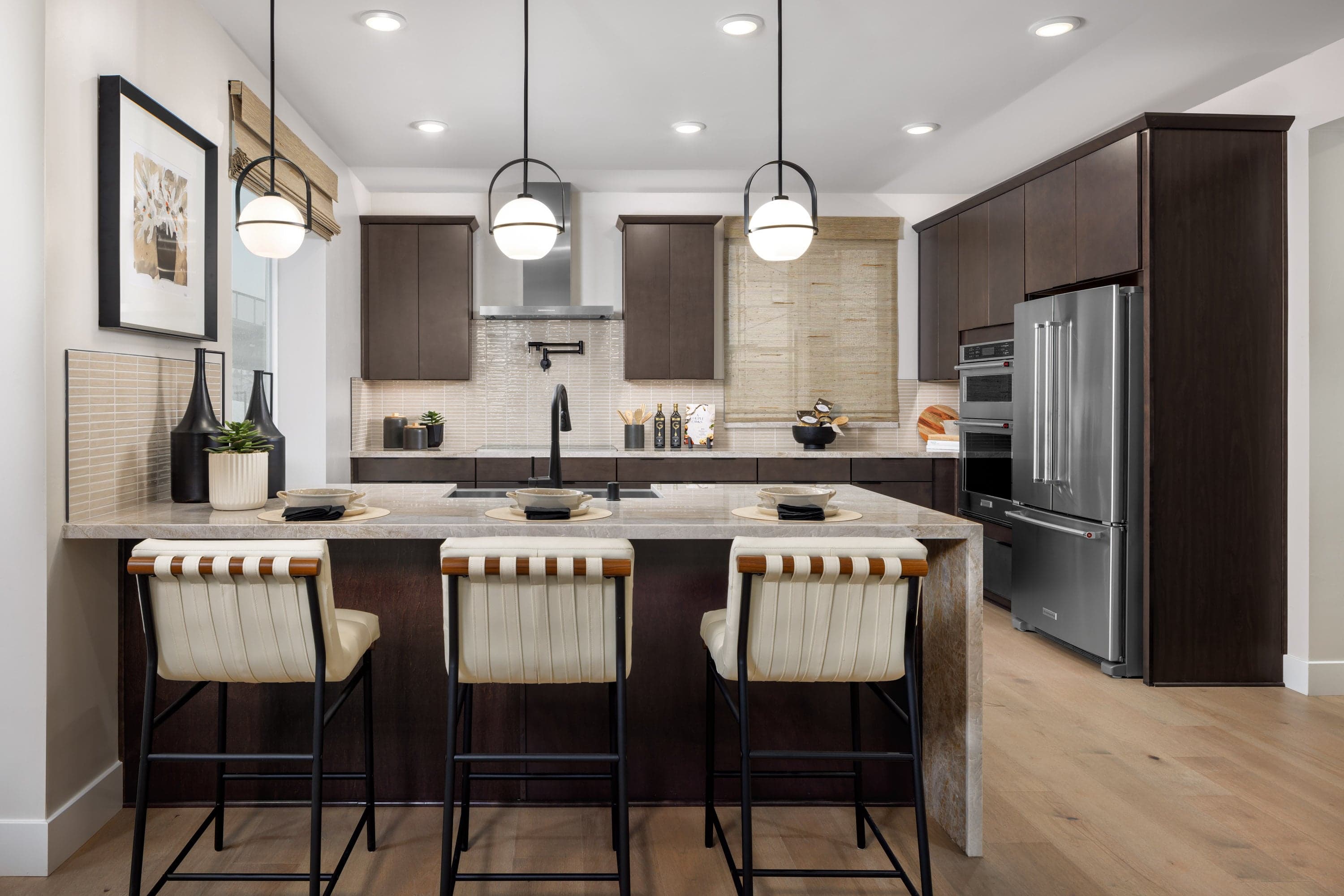kitchen with espresso cabinets, light wood floors, stainless steel appliances, and three white stools at counter