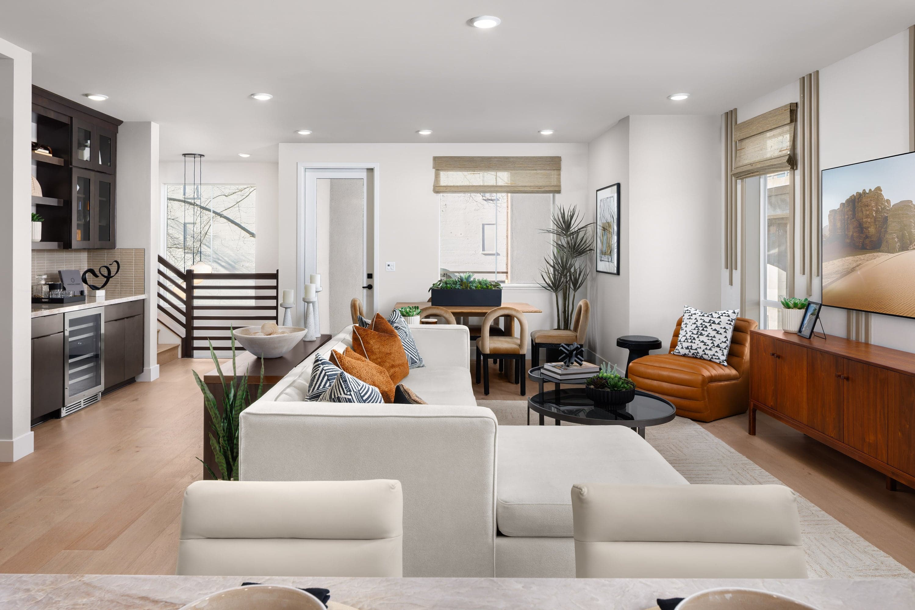 great room with wood floors, white sofa with orange pillows, cognac leather chair, beverage bar with espresso cabinets & mini fridge, and multiple windows
