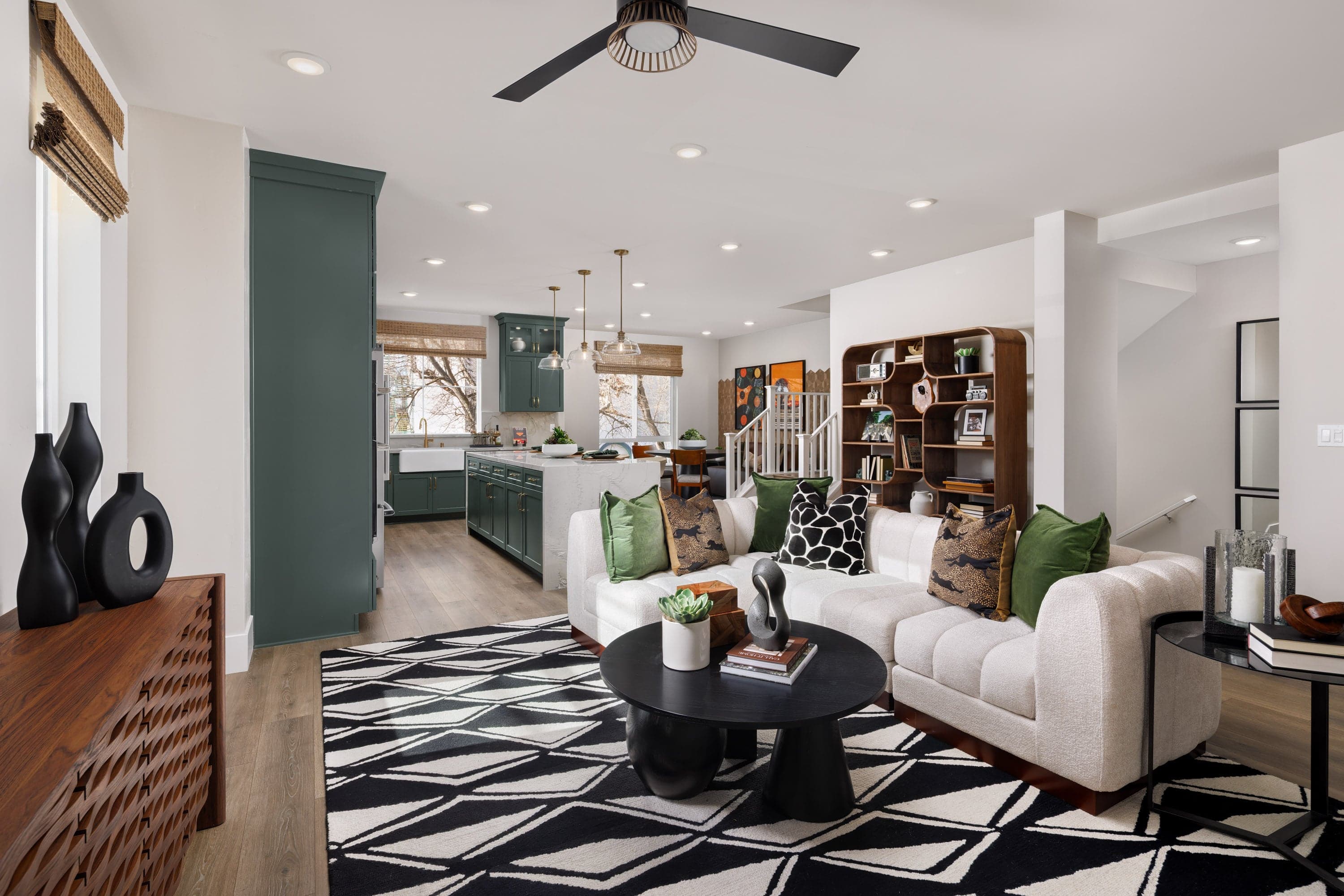 great room with wood floors, black & white modern patterned area rug, white sofa, and view of kitchen with green cabinets