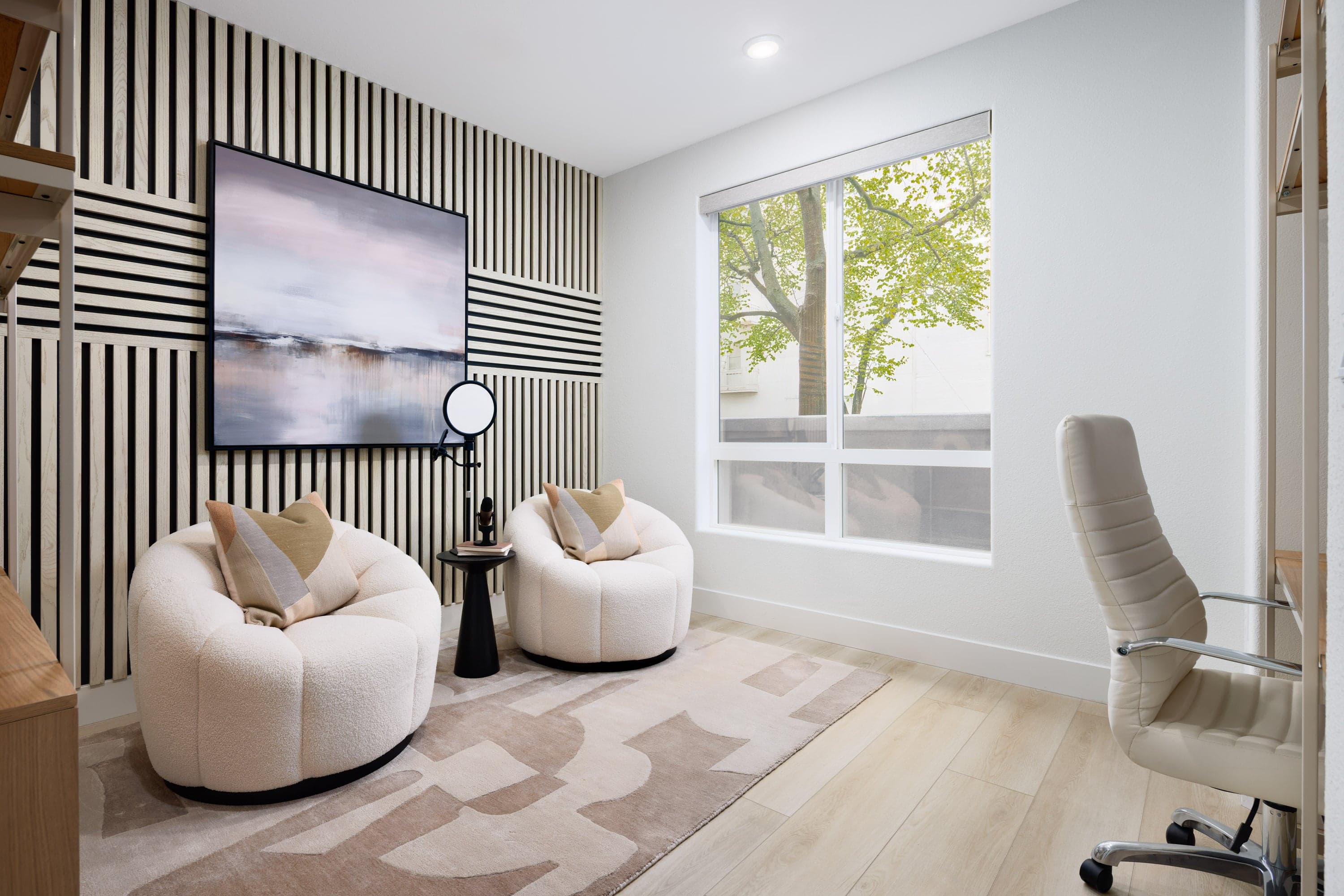 study with large window, light wood floors, two white club accent chairs, black & white wood paneled wall, and bookshelves