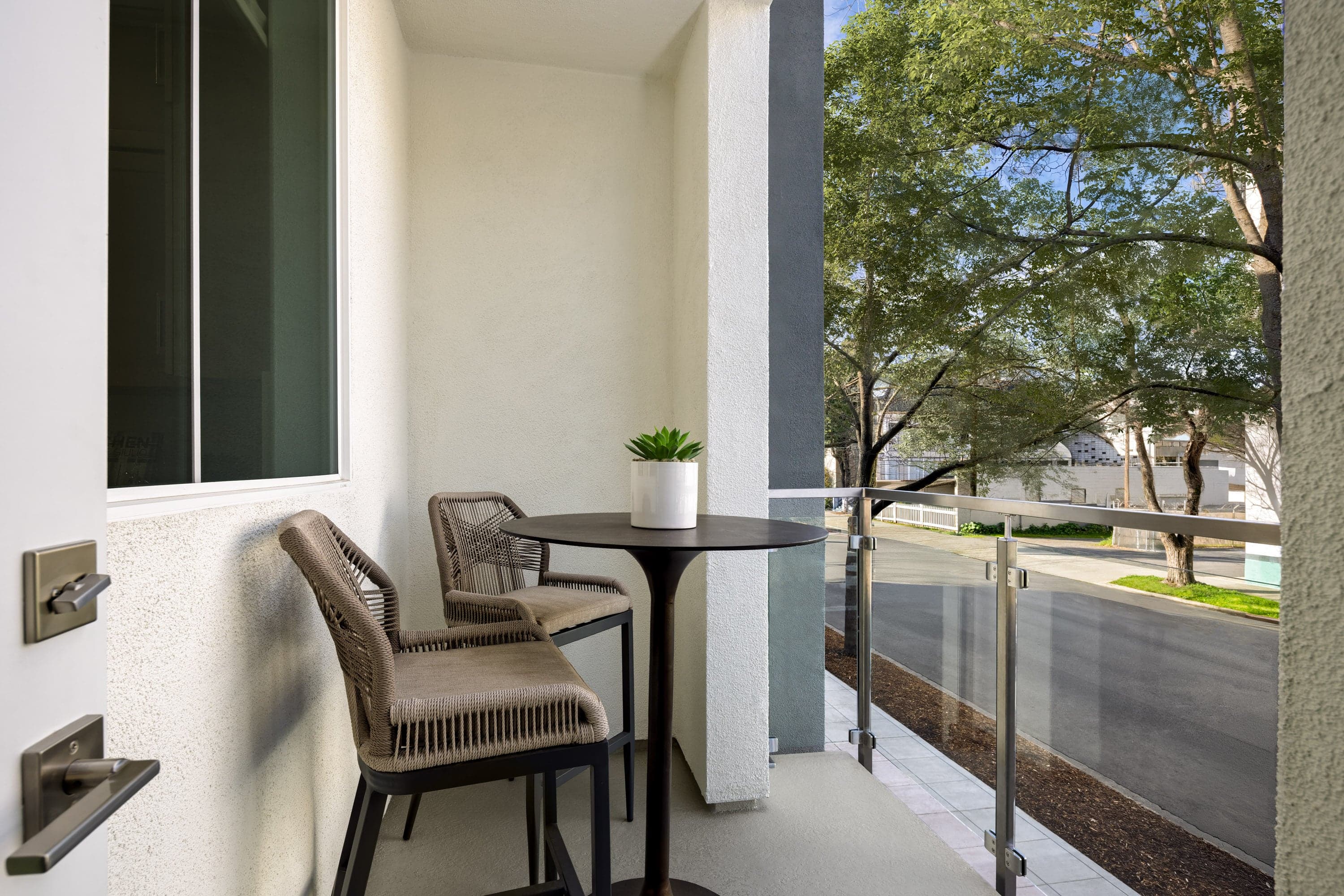 covered second story deck with black pub table, two tan barstools, and view of trees & street