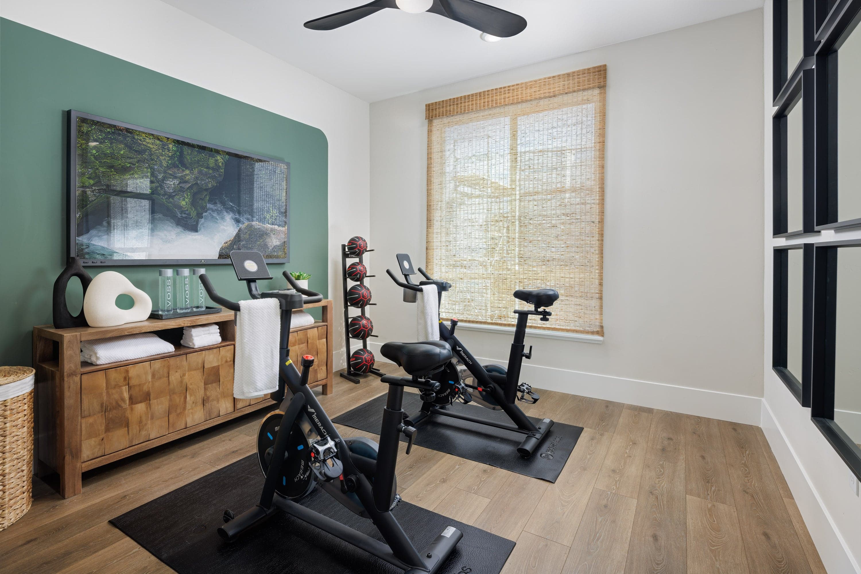 room with two stationary exercise bikes, wood floors, green wall behind television, and window