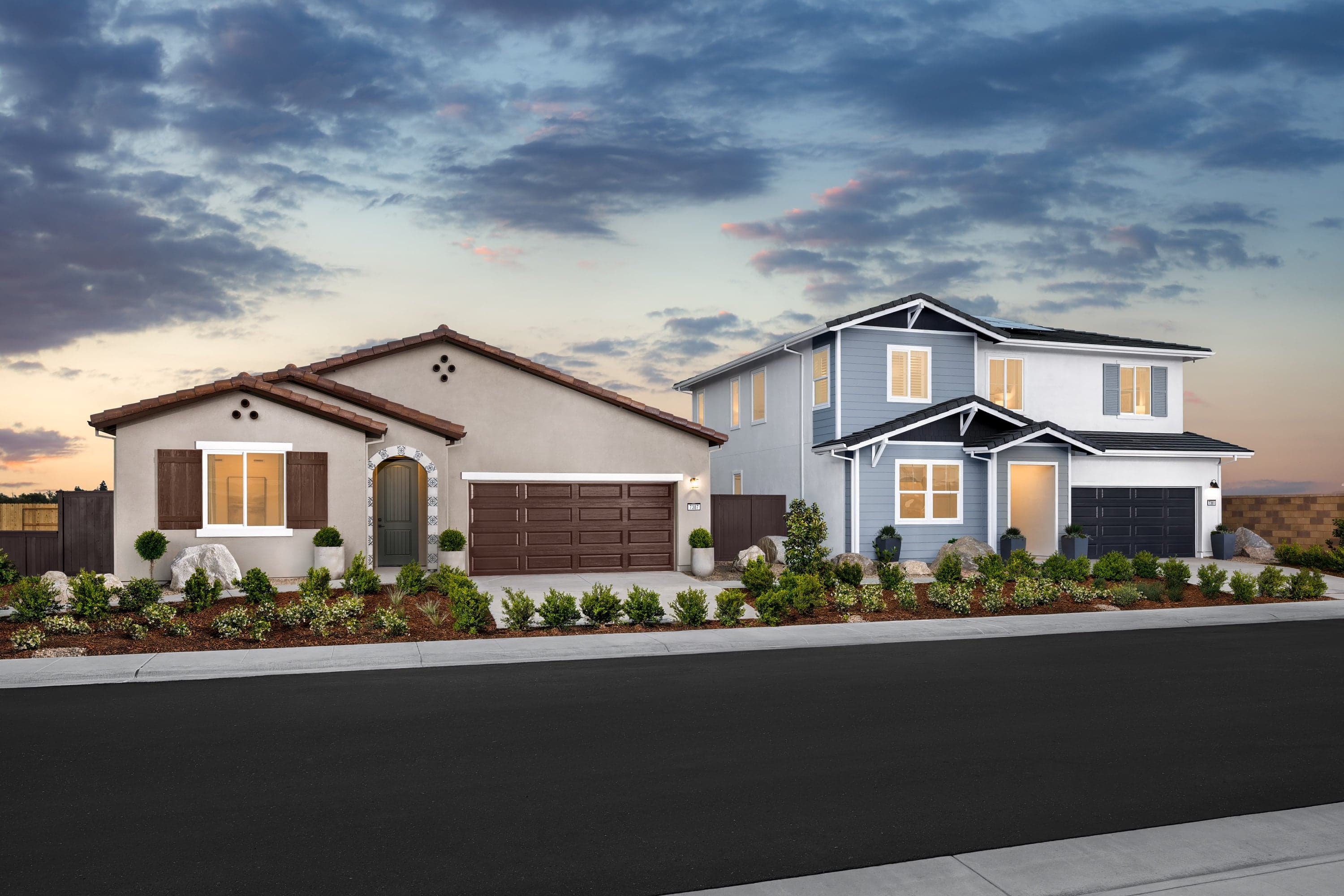 front exteriors of single-story brown spanish style home and gray two-story home at dusk