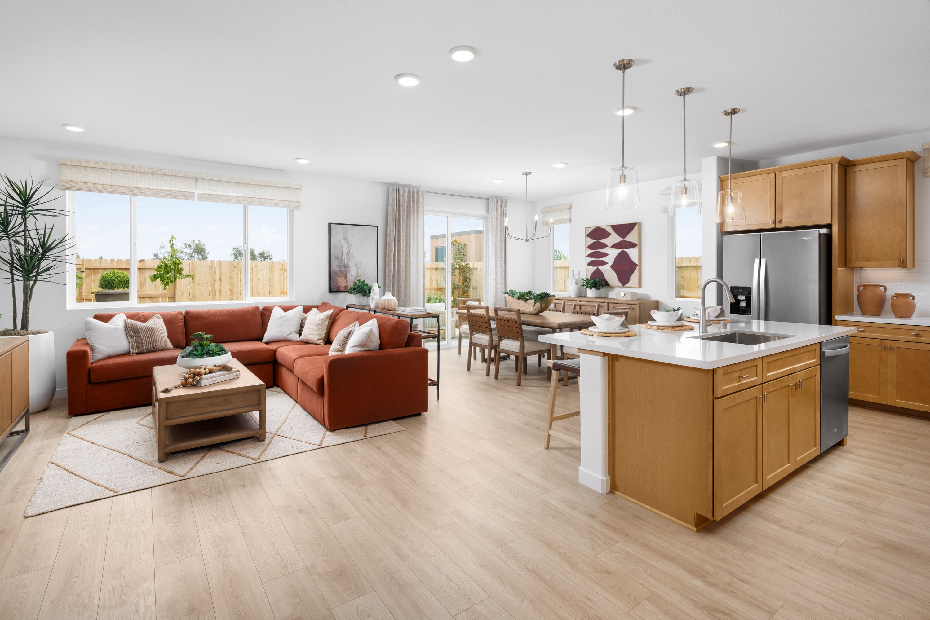 great room with light wood floors, rust sectional sofa, and large window looking out to the backyard