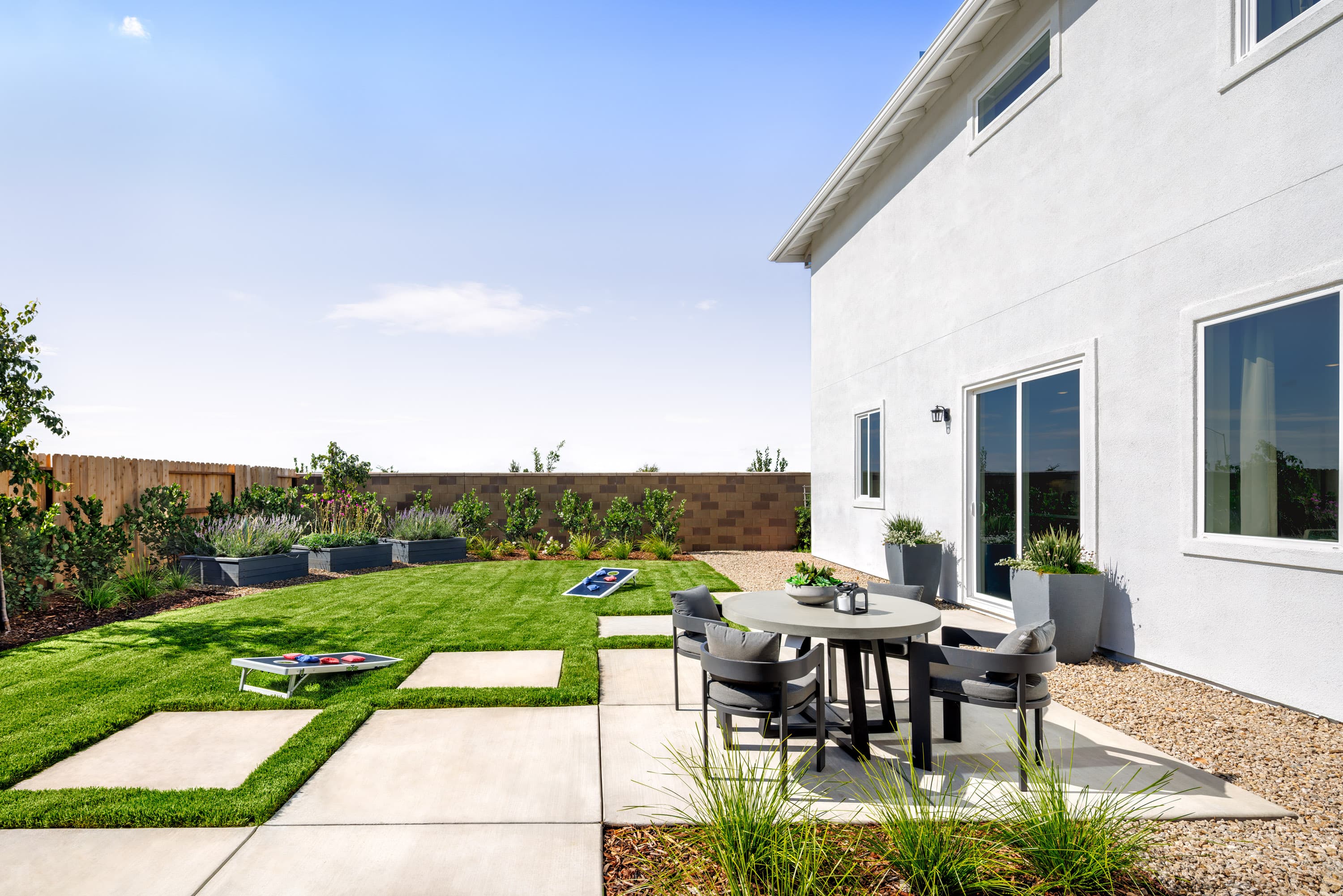 backyard with grass, concrete patio with round table & chairs, and raised garden beds