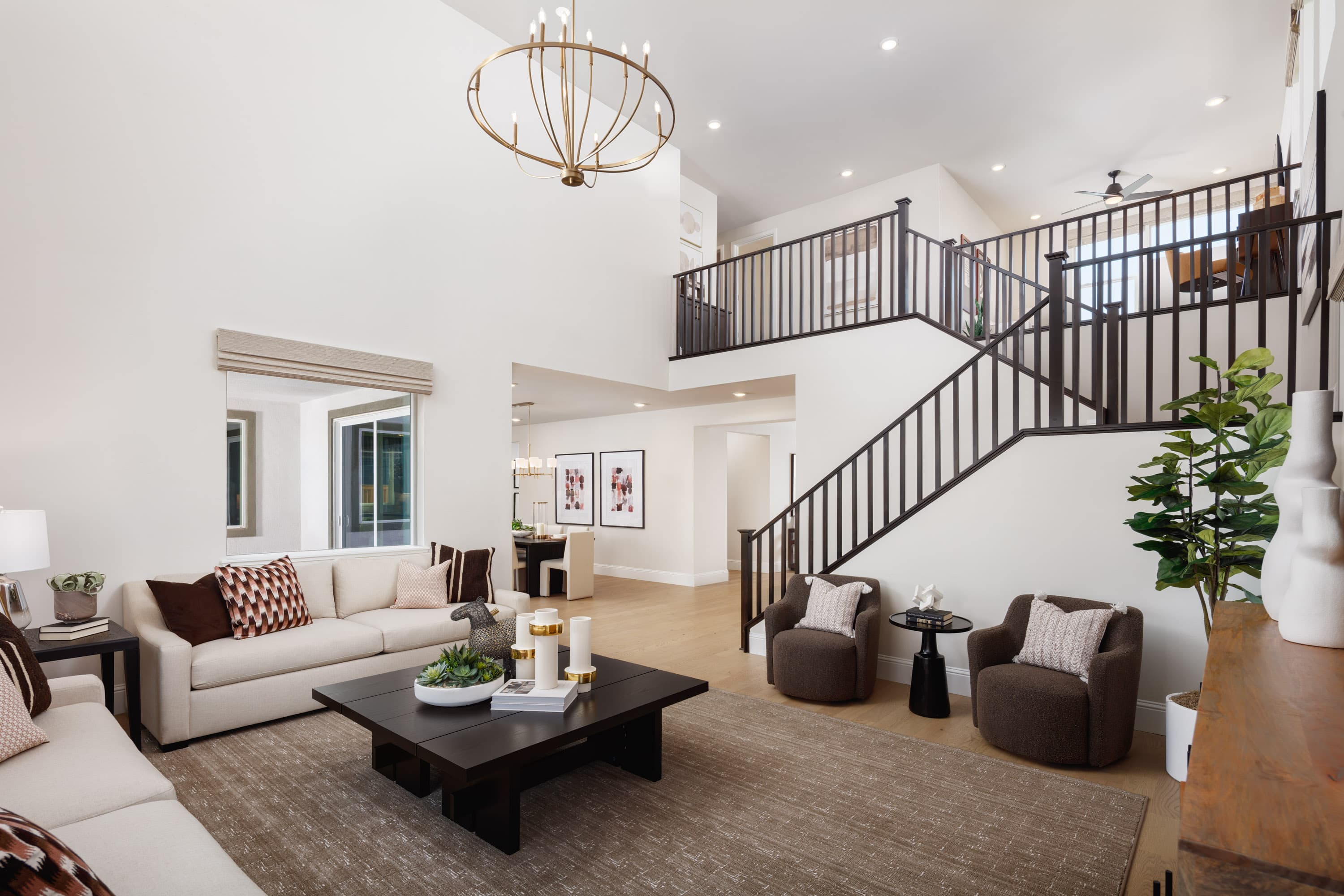 great room with two-story volume ceiling, wood floors, dark wood coffee table, two white sofas, and two brown chairs