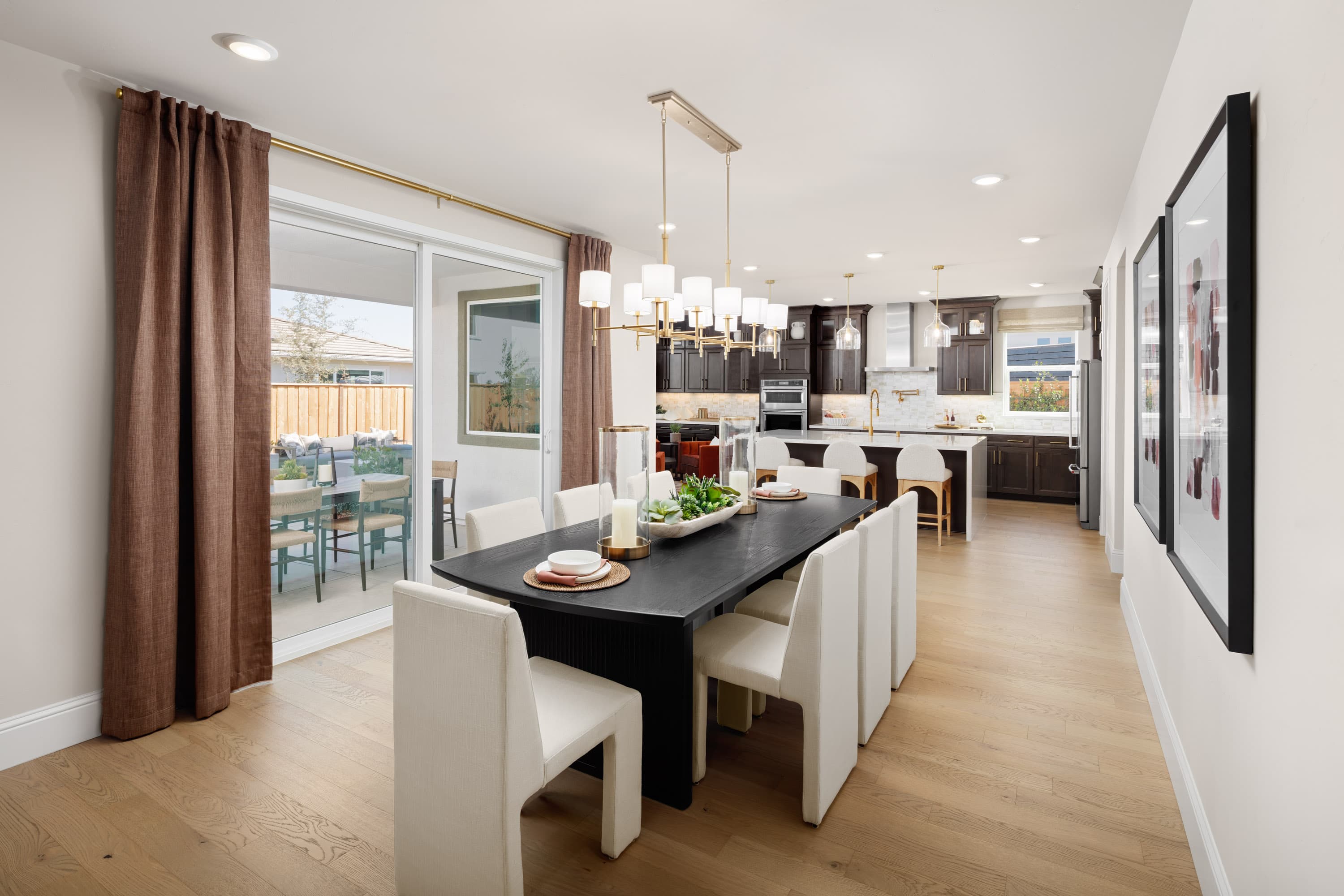 dining room with wood floors, black table with eight white chairs, sliding glass door to back patio, and brown curtains